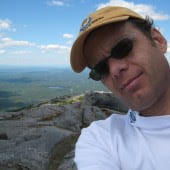 selfie of joseph moore in yellow hat on  a mountain summit